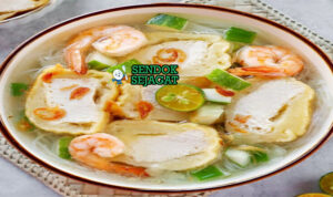 Mangkuk model khas Palembang dengan adonan ikan kenyal isi tahu, disiram kuah kaldu udang bening, taburan seledri, daun bawang, bawang goreng, dan soun