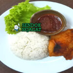 Porsi nasi katok khas Brunei dengan nasi putih hangat, potongan ayam goreng kecokelatan, telur mata sapi setengah matang, siraman sambal pedas manis, dan irisan timun segar