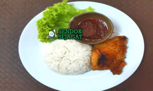Porsi nasi katok khas Brunei dengan nasi putih hangat, potongan ayam goreng kecokelatan, telur mata sapi setengah matang, siraman sambal pedas manis, dan irisan timun segar