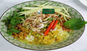 Nom Banh Chok khas Kamboja disajikan hangat dengan mie beras, kuah santan ikan kuning kehijauan, sayur mentah renyah, dan daun harum