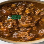 Oxtail stew khas Jamaica siap saji: potongan ekor sapi empuk lepas tulang dalam kuah kental cokelat gelap, butter beans, thyme, dan hint pedas Scotch bonnet, terlihat menggoda dengan uap hangat