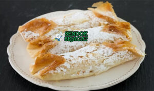 Pastéis de Tentúgal khas Portugal siap saji: pastel kecil berbentuk tabung dengan kulit pastry tipis renyah kecokelatan, isian custard telur kuning lumer mengalir saat dipotong, tabur gula halus, terlihat manis menggoda di piring putih