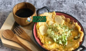 Potongan pempek lenggang khas Palembang yang lembut bertekstur fluffy, disajikan dengan cuko hitam pedas, irisan timun segar, bawang goreng, dan ebi sangrai