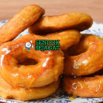 Tumpukan Picarones khas Peru yang renyah keemasan, direndam sirup chancaca mengkilap, tampak manis gurih menggugah selera