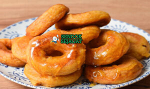 Picarones Siap Nikmati dengan Sirup Chancaca Tumpukan Picarones khas Peru yang renyah keemasan, direndam sirup chancaca mengkilap, tampak manis gurih menggugah selera