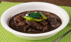 Pork dinuguan khas Filipina siap saji: sup darah babi hitam pekat gurih, potongan daging empuk, cabai hijau iris, dan kuah kental mengkilap, terlihat hangat menggoda dengan nasi putih