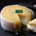 Queijo da Serra khas Portugal siap saji: keju domba lembut krimy berwarna putih krem, tekstur kental lumer, dipotong memperlihatkan bagian dalam halus, disajikan dengan roti gandum dan madu, terlihat gurih menggoda