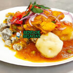 Sajta de Pollo khas Bolivia disajikan hangat dalam mangkuk dengan potongan ayam empuk, kuah pedas kuning dari ají amarillo, kentang, kacang polong, dan nasi putih