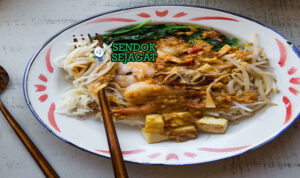 Satay bee hoon khas Singapura siap saji: mangkuk bihun lembut dengan kuah sate kacang manis gurih berwarna cokelat kental, udang panggang besar, tauge segar, telur rebus, tahu goreng, bawang goreng, dan limau kasturi, terlihat menggoda dengan uap hangat