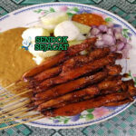 Sate Ayam Ponorogo Siap Disantap Hangat Tusuk sate ayam Ponorogo khas Jawa Timur dengan daging empuk berbalut bumbu kacang manis gurih kental, taburan bawang goreng melimpah, disajikan bersama lontong, kol iris, dan sambal kecap