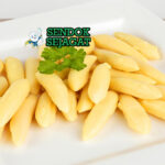 Piring schupfnudeln khas Austria berbentuk lonjong kecokelatan renyah, disiram mentega cokelat harum, taburan bawang goreng dan peterseli segar, disajikan hangat