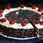 Potongan kue Schwarzwälder Kirschtorte khas Jerman menampilkan lapisan sponge cokelat lembut, whipped cream putih, filling ceri merah, dan taburan serutan cokelat gelap
