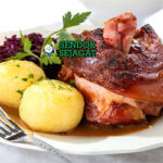 Schweinshaxe khas Jerman dengan kulit renyah keemasan menggelembung, daging empuk di bawahnya, disajikan dengan sauerkraut dan bir, tampak gurih dan menggugah selera