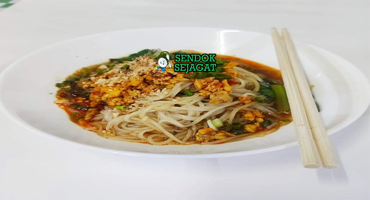 Shan noodles khas Myanmar siap saji: mangkuk mie beras kenyal dengan kuah tomat kacang tanah kental berwarna merah kecokelatan, daging cincang gurih, telur rebus, tauge segar, bawang goreng, kacang tanah cincang, daun bawang iris, dan jeruk nipis, terlihat hangat menggoda dengan uap mengepul