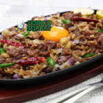 Sizzling Pork Sisig Panas di Hot Plate dengan Cabai dan Jeruk Nipis Sizzling pork sisig khas Filipina siap saji: daging babi cincang renyah di hot plate besi panas, bawang bombay segar, cabai rawit merah, jeruk nipis peras, uap mengepul dan bunyi sizzling menggoda