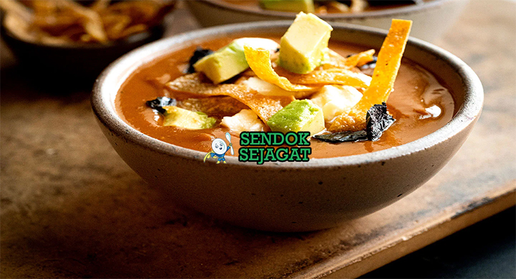 Sopa Tarasca khas Meksiko siap saji: mangkuk sup kacang hitam kental berwarna hitam kecokelatan, tabur tortilla goreng renyah, alpukat iris, keju cotija parut, krim asam, bawang merah, daun ketumbar segar, terlihat gurih pedas hangat dengan uap mengepul