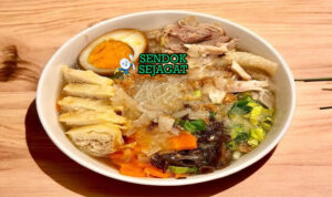 Mangkuk timlo khas Solo berisi kuah kaldu bening harum, suwiran ayam lembut, telur pindang kecokelatan, soun kenyal, wortel, jamur kuping, taburan bawang goreng dan daun bawang