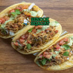 Tinga de pollo khas Meksiko siap saji: ayam suwir empuk dalam saus tomat merah pedas chipotle, bawang bombay karamel, disajikan dengan tortilla jagung hangat, alpukat iris, krim asam, keju cotija, dan jeruk nipis, terlihat gurih menggoda