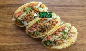 Tinga de pollo khas Meksiko siap saji: ayam suwir empuk dalam saus tomat merah pedas chipotle, bawang bombay karamel, disajikan dengan tortilla jagung hangat, alpukat iris, krim asam, keju cotija, dan jeruk nipis, terlihat gurih menggoda