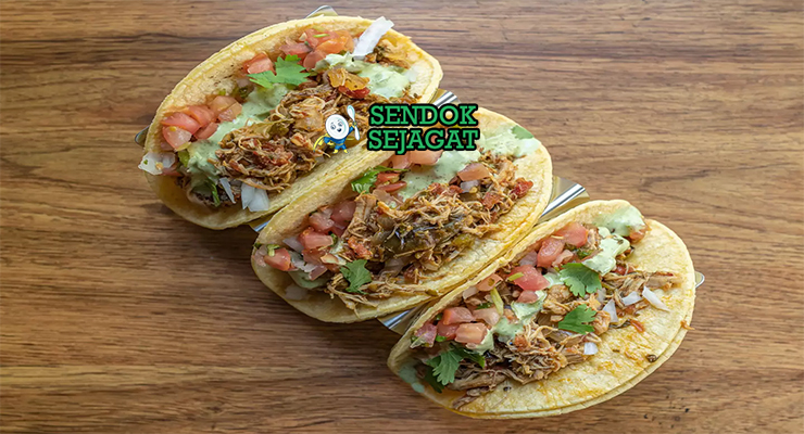 Tinga de pollo khas Meksiko siap saji: ayam suwir empuk dalam saus tomat merah pedas chipotle, bawang bombay karamel, disajikan dengan tortilla jagung hangat, alpukat iris, krim asam, keju cotija, dan jeruk nipis, terlihat gurih menggoda