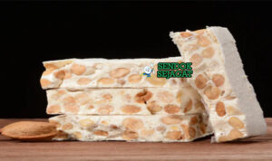 Turrón Alicante Potong Siap Sajikan dengan Almond Utuh Renyah Turrón khas Spanyol siap saji: blok nougat keras Alicante dengan almond utuh terlihat renyah, madu mengkilap, potong kotak di piring kayu, terasa manis dan crunchy