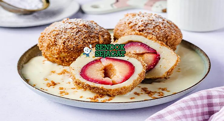 Zwetschgenknödel khas Austria berbentuk lonjong kecokelatan renyah, di atas piring dengan mentega cokelat harum, taburan gula kayu manis dan gula bubuk, potongan plum terlihat di dalam