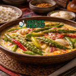 Ema Datshi khas Bhutan dengan cabai hijau empuk diselimuti saus keju creamy pedas, disajikan hangat di mangkuk bersama nasi merah Bhutan