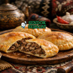 Pie ichlekli Turkmenistan berwarna kecokelatan renyah, dipotong menunjukkan isi daging juicy dengan tomat dan paprika di piring putih