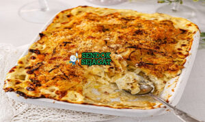 Janssons Frestelse khas Swedia dengan lapisan kentang iris lembut, anchovy gurih, bawang karamel, atas roti parut kecokelatan renyah, tampak kremi hangat menggugah selera