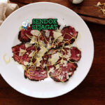 Kangaroo Carpaccio khas Australia dengan irisan daging kanguru mentah tipis merah muda, black garlic umami, minyak zaitun, tampak segar gurih menggugah selera