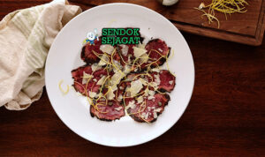 Kangaroo Carpaccio khas Australia dengan irisan daging kanguru mentah tipis merah muda, black garlic umami, minyak zaitun, tampak segar gurih menggugah selera