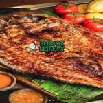 Masgouf Siap Saji Panas Masgouf khas Irak dengan ikan mas panggang terbuka renyah kecokelatan, asap kayu bakar, tampak gurih hangat menggugah selera