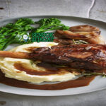 Saltbush Lamb Shanks khas Australia dengan kaki domba empuk meleleh dari tulang, saus kental rempah bush, tampak gurih hangat menggugah selera