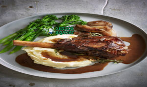 Saltbush Lamb Shanks khas Australia dengan kaki domba empuk meleleh dari tulang, saus kental rempah bush, tampak gurih hangat menggugah selera