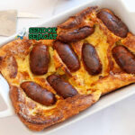 Toad in the Hole khas Britania dengan sosis terbenam dalam adonan Yorkshire pudding mengembang tinggi emas, tampak gurih hangat menggugah selera