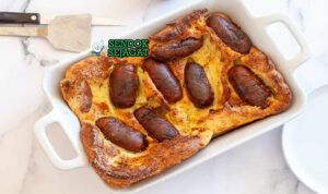 Toad in the Hole khas Britania dengan sosis terbenam dalam adonan Yorkshire pudding mengembang tinggi emas, tampak gurih hangat menggugah selera
