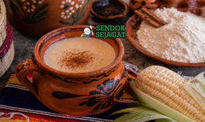 Minuman kental berwarna krem dalam cangkir dengan batang kayu manis dan uap hangat yang menggoda