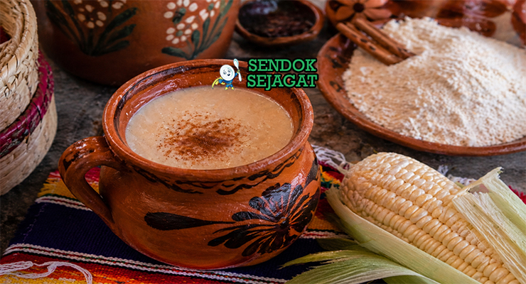 Minuman kental berwarna krem dalam cangkir dengan batang kayu manis dan uap hangat yang menggoda