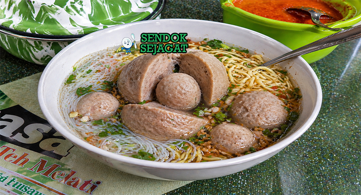 Bakso beranak berukuran besar dalam mangkuk dengan kuah kaldu bening, dibelah memperlihatkan bakso kecil di dalamnya, lengkap dengan mie, daun bawang, dan taburan seledri
