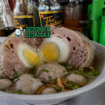 Semangkuk bakso telur khas Tasikmalaya dengan kuah bening, bakso besar berisi telur kuning di tengah, taburan daun bawang dan bawang goreng, tampilan hangat dan menggugah selera