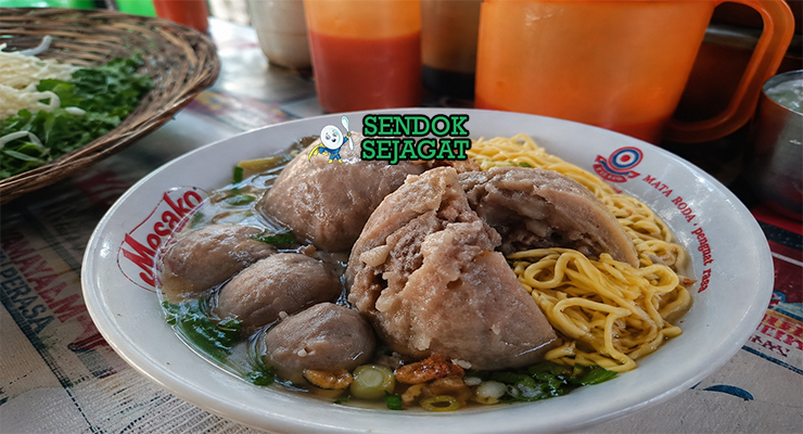 Bakso berwarna cokelat muda dengan potongan urat di dalamnya, disajikan dalam kuah bening dengan daun bawang dan bawang goreng