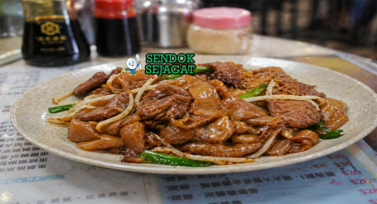 Hidangan beef chow fun dengan mie lebar berwarna cokelat mengilap, irisan daging sapi juicy, tauge segar, dan daun bawang dalam wajan panas