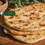 Flatbread panggang dengan tekstur sedikit gosong di tepi, topping bush tomato dan rempah, tampilan rustic khas gurun Australia