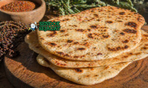 Flatbread panggang dengan tekstur sedikit gosong di tepi, topping bush tomato dan rempah, tampilan rustic khas gurun Australia