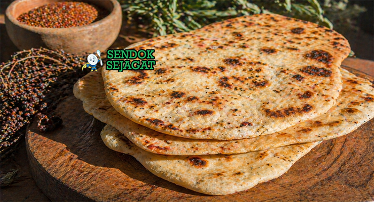 Flatbread panggang dengan tekstur sedikit gosong di tepi, topping bush tomato dan rempah, tampilan rustic khas gurun Australia