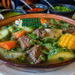 Sup bening dengan potongan daging sapi, jagung, wortel, kentang, dan zucchini dalam mangkuk hangat