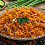 Dambu Nama khas Nigeria berupa serpihan daging sapi kering berwarna cokelat keemasan dengan tekstur halus dan berserat, terlihat gurih dan berbumbu kuat dalam mangkuk tradisional