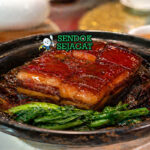 Dong po rou dalam piring saji dengan potongan daging perut babi empuk, kulit kenyal, dan saus kecokelatan kental, ditemani nasi putih