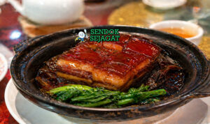 Dong po rou dalam piring saji dengan potongan daging perut babi empuk, kulit kenyal, dan saus kecokelatan kental, ditemani nasi putih