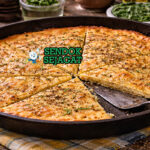 Potongan farinata khas Genoa dengan pinggir renyah keemasan, permukaan berkilau minyak zaitun, dan taburan lada hitam, disajikan di piring kayu